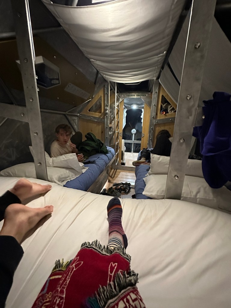 Interior view of a cozy sleeping capsule at Starlodge in the Sacred Valley, Peru, featuring beds with blue linens and several guests relaxing.