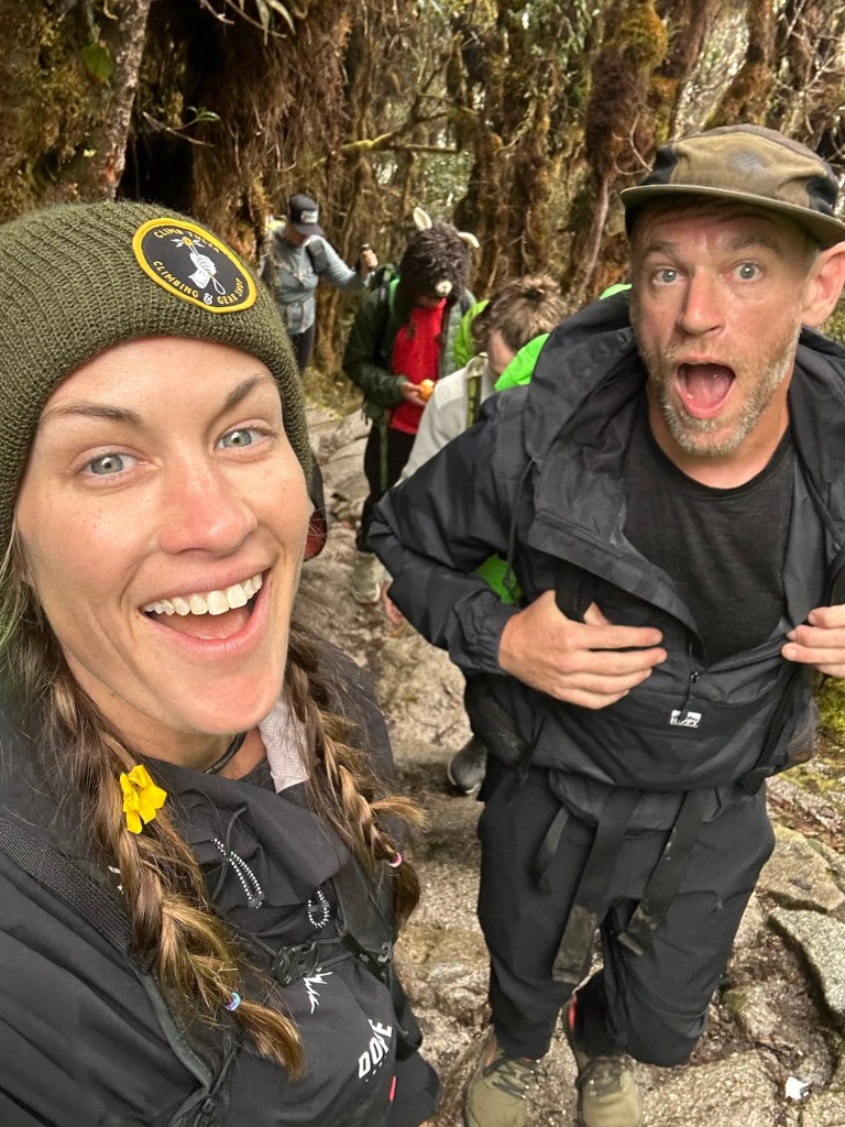 A group of hikers, including a man and woman, posing for a selfie on a forest trail, surrounded by lush greenery.