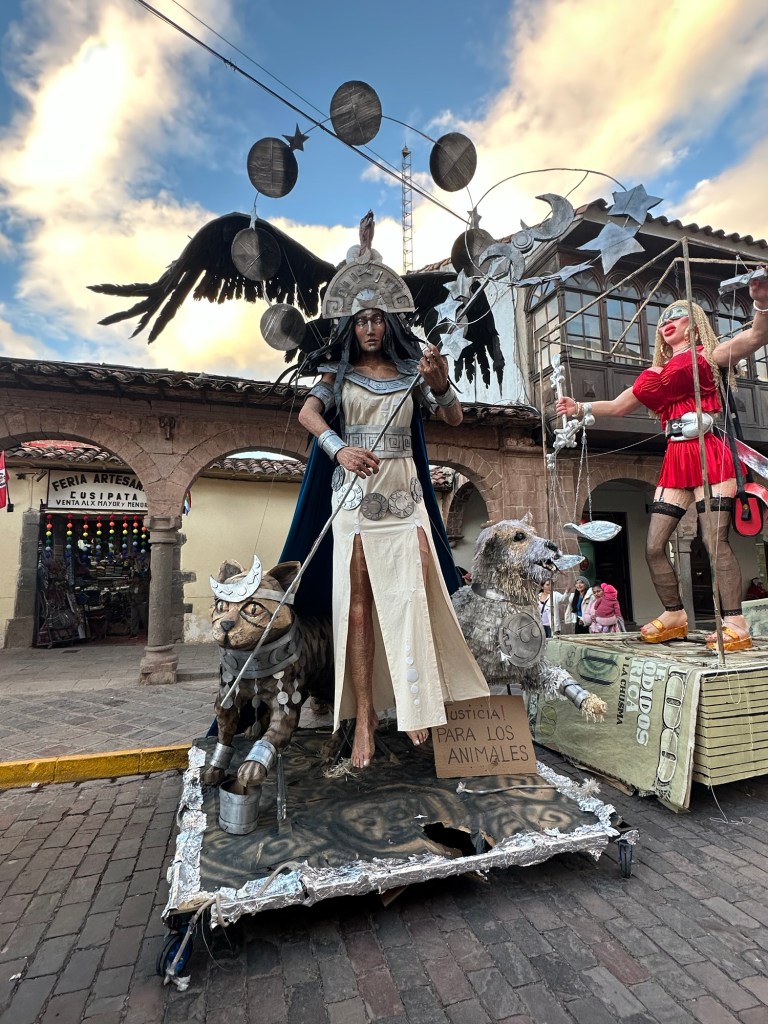 A street performance depicting a character dressed in silver armor with animal companions, set against a colorful sky in Cusco.