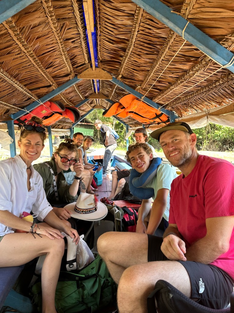 A group of travelers sitting inside a boat with a thatched roof, surrounded by natural scenery, preparing for an adventure in the Amazon jungle.