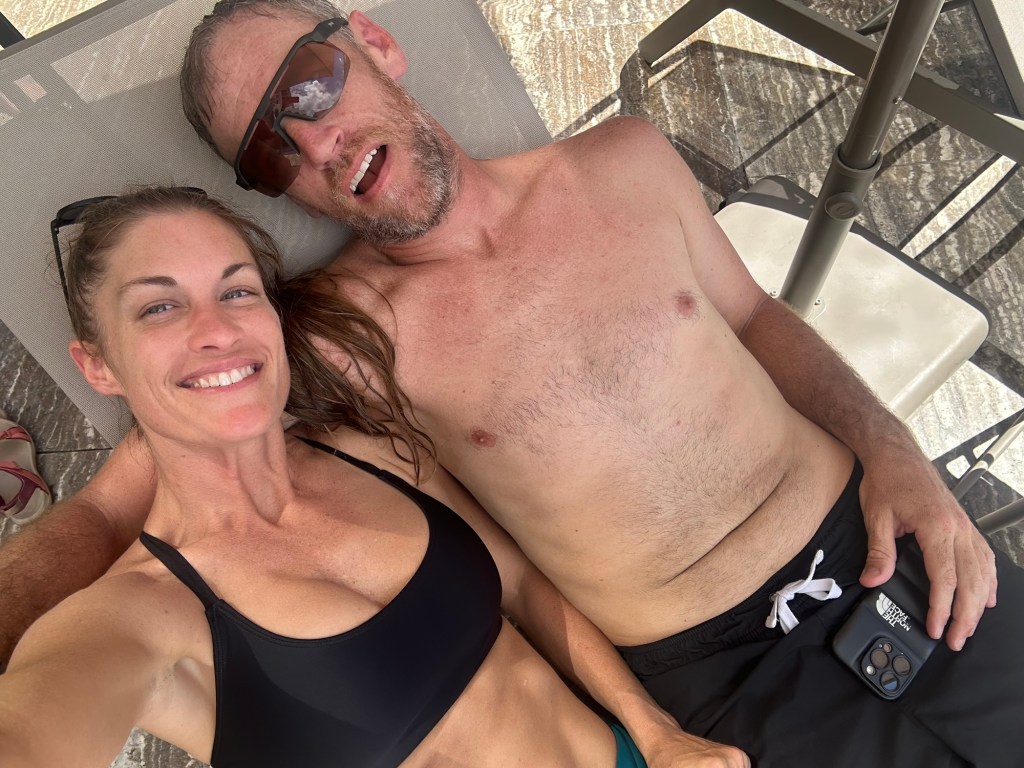 A couple taking a selfie while relaxing outside, smiling and enjoying their time together in swimwear.