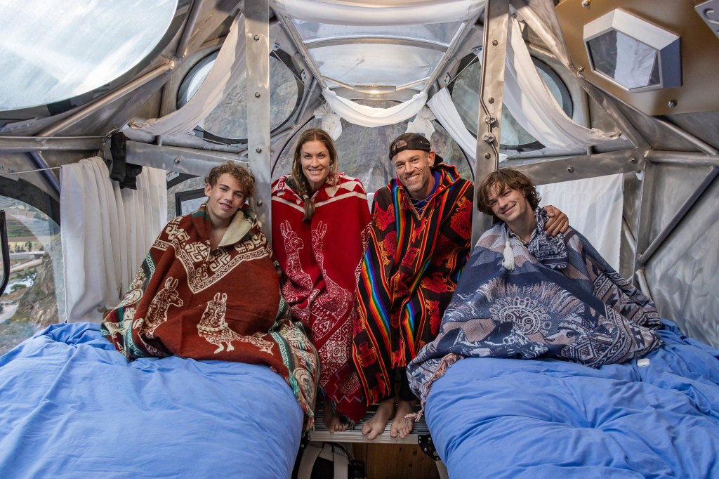 Family enjoying a cozy moment inside a unique capsule hotel in the Sacred Valley, Peru, wrapped in colorful blankets.
